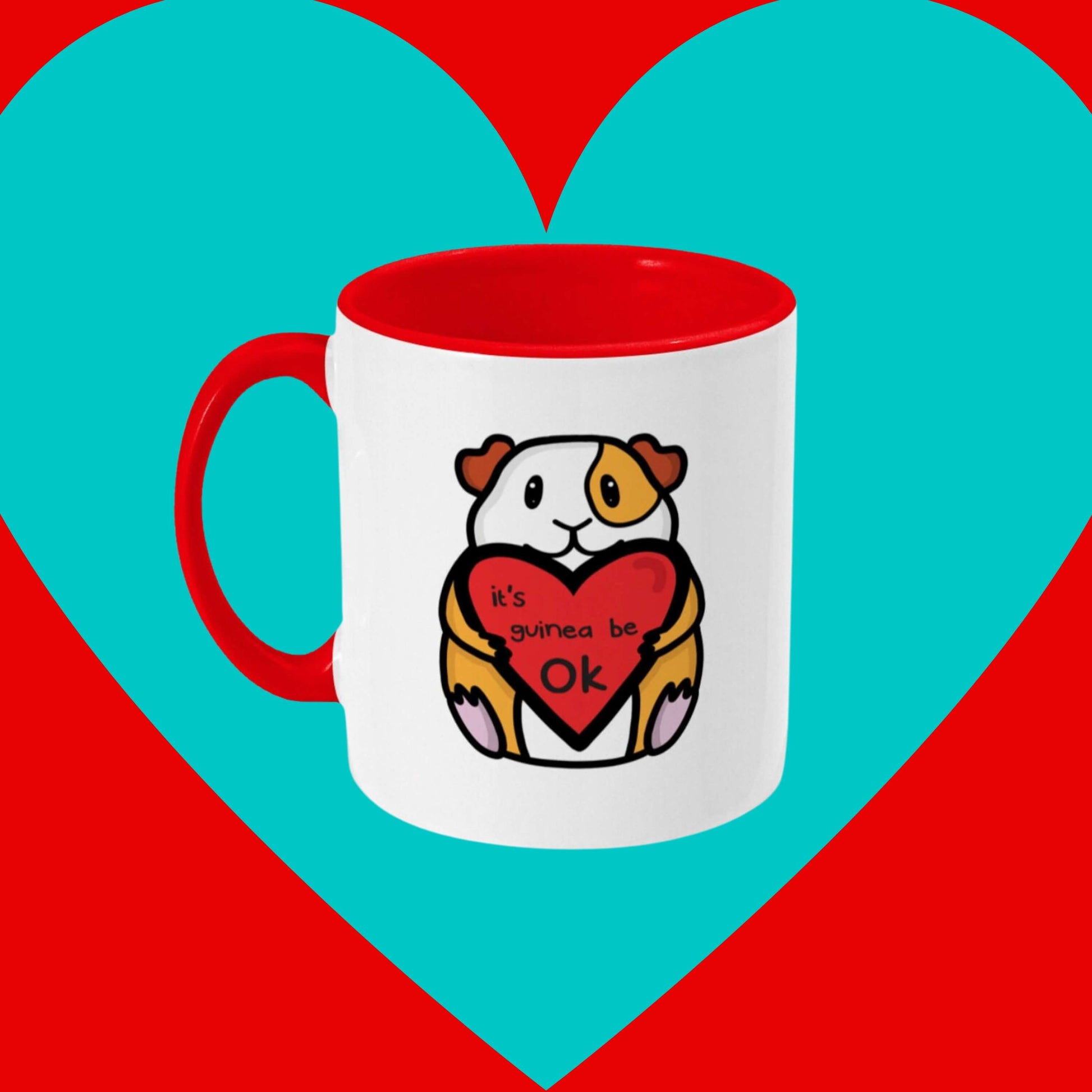 The It's Gonna Be OK Guinea Pig Mug on a red and blue background. The white mug has a red inside and handle with a front print of a orange and white guinea pig smiling holding a red heart with black text reading 'it's guinea be ok'. The hand drawn design is a reminder of staying positive.