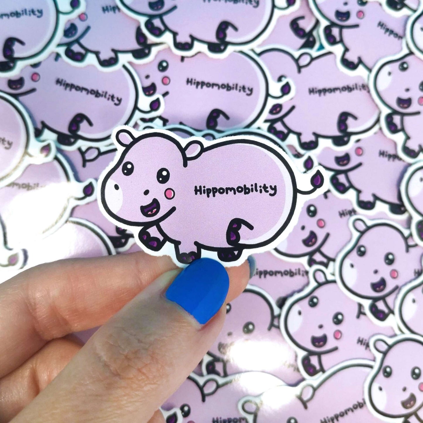 Hippomobility Sticker - Hyper Mobility held over other multiple copies of the same sticker. A cute smiling pastel purple hippo flicking its back leg up with black text reading 'hippomobility' across its body. The hand drawn design is raising awareness for hyper mobility and EDS.