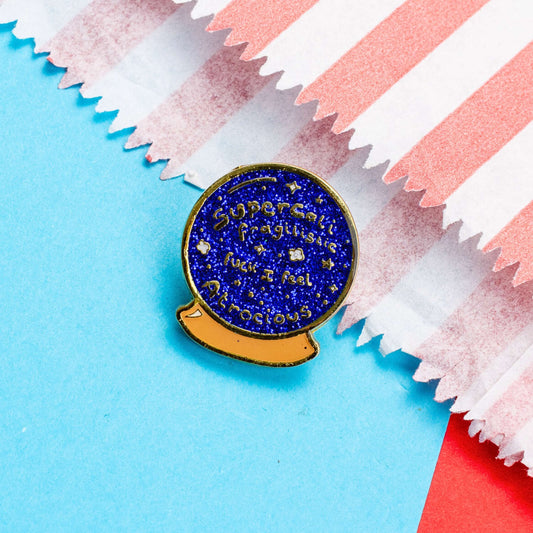 I Feel Atrocious Enamel Pin - Blue circle crystal ball shaped enamel pin with gold text reading 'supercali fragilistic fuck I feel atrocious' on. It is on a red and blue card background. Enamel pin designed to raise awareness for invisible illnesses.