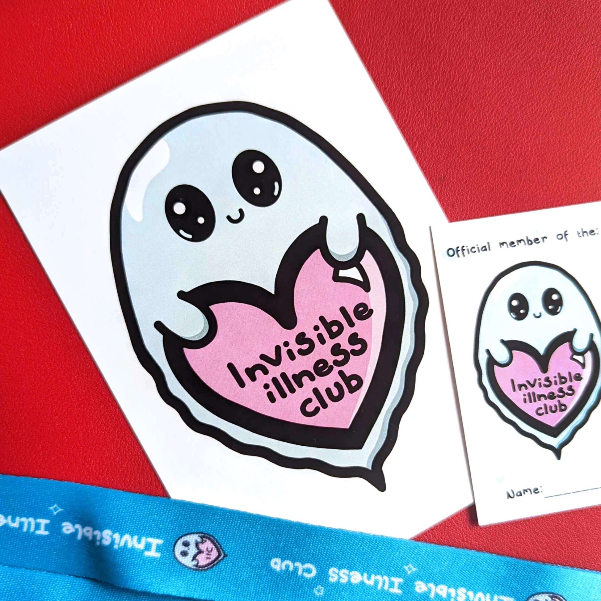 Close up of Invisible Illness Club postcard which is white with and an illustration of a cute mint green ghost with big eyes and little smile holding a pink heart with it's little hands that has 'invisible illness club' written in black writing in the middle of the heart underneath.