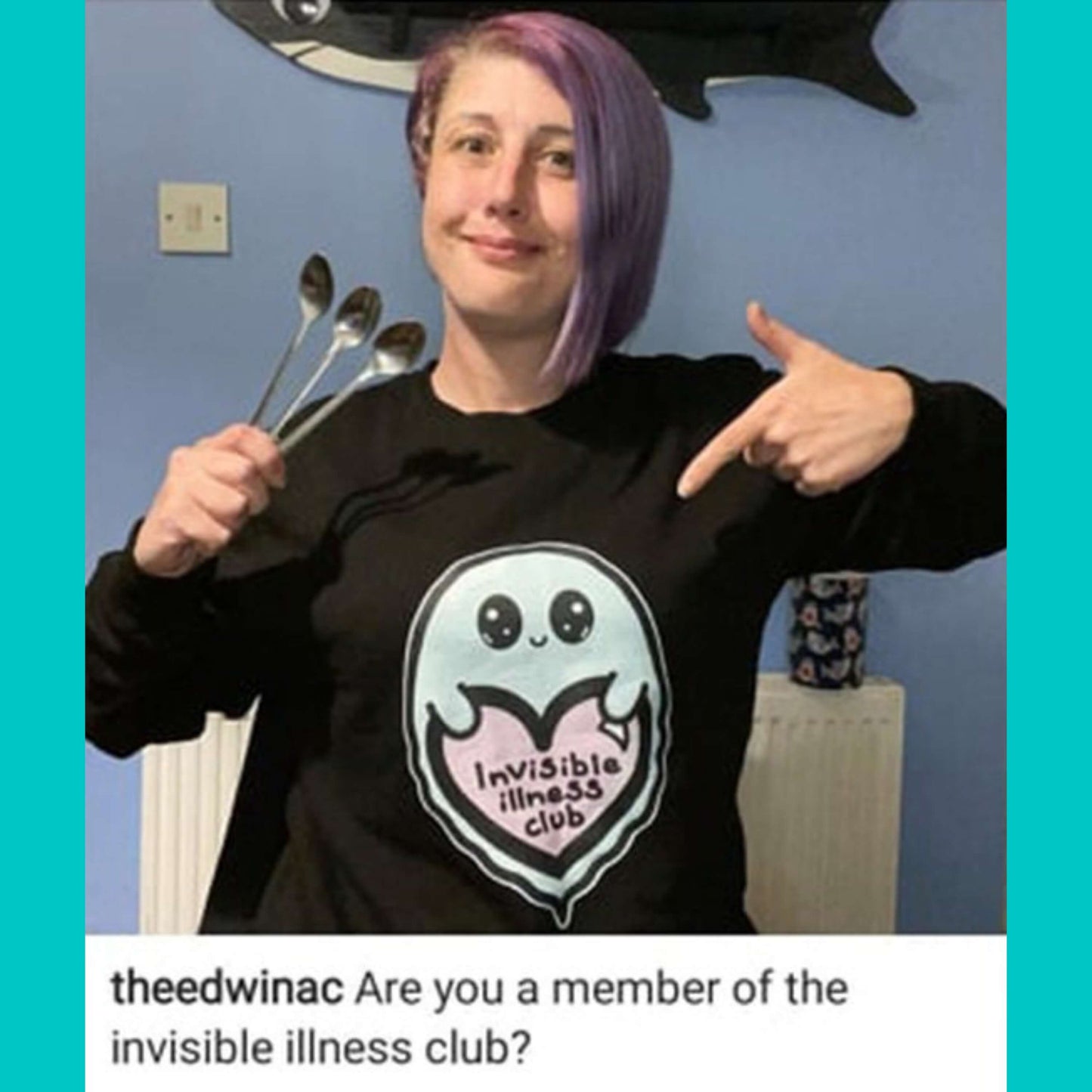 The Invisible Illness Club Sweatshirt Jumper being modelled by @theedwinac in front of a purple wall, she has a purple asymmetric bob and is smiling pointing down at the jumper and holding up 3 spoons. The black sweater features a smiling pastel blue ghost with big sparkly eyes holding up a pastel pink heart with black text reading 'invisible illness club'. The hand drawn design is raising awareness for hidden disabilities.