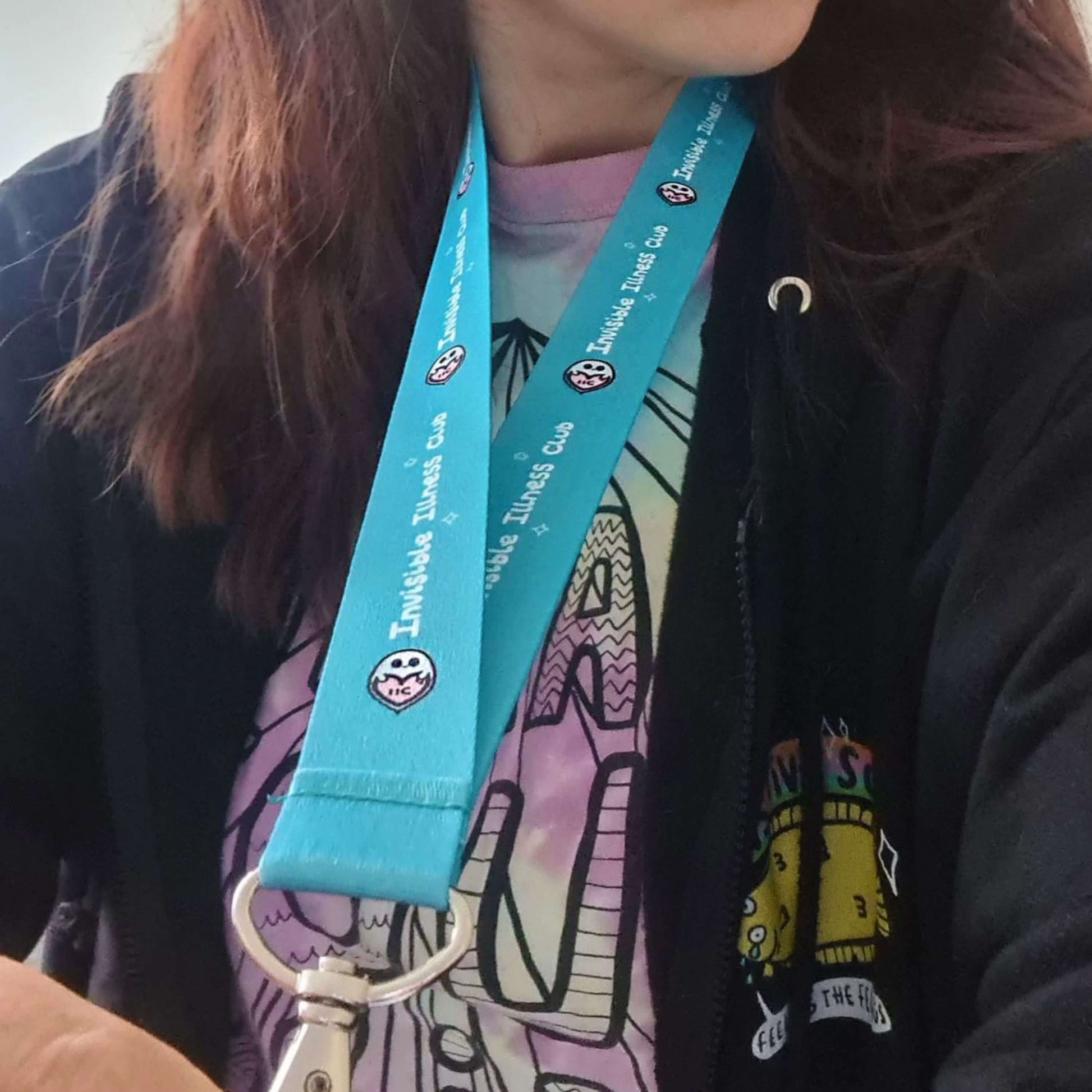 The Invisible Illness Club Lanyard modelled by Nikky (innabox owner) wearing a katie abey rainbow tshirt and black katie abey hoodie. The pastel blue lanyard has repeating white text reading 'invisible illness club' and innabox pastel ghost logo. It has a silver lobster clip and white safety break. The hand drawn design is raising awareness for hidden disabilities.