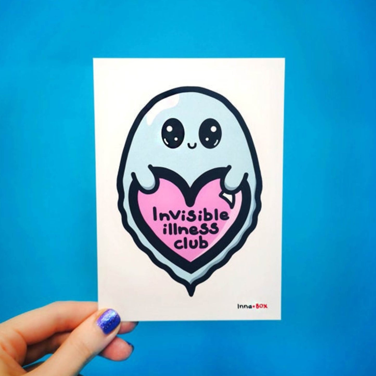 The Invisible Illness Club Postcard held over a blue background. The white postcard print features a pastel blue smiling ghost with big sparkly eyes holding up a pink heart with black text reading 'invisible illness club' with the innabox logo in the bottom right corner. The hand drawn design is raising awareness for hidden disabilities and chronic illness.