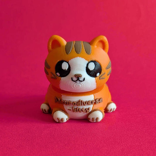 Front view of Innabox Neurodiverse Kitty Desk Buddy fidget toy in orange and brown, with large glossy eyes and “Neurodiverse Kitty” text on its tummy, placed against a bright red background. Palm sized 3D printed sensory desk companion made from biodegradable PLA, designed to support autism, anxiety, chronic illness and hidden disabilities.