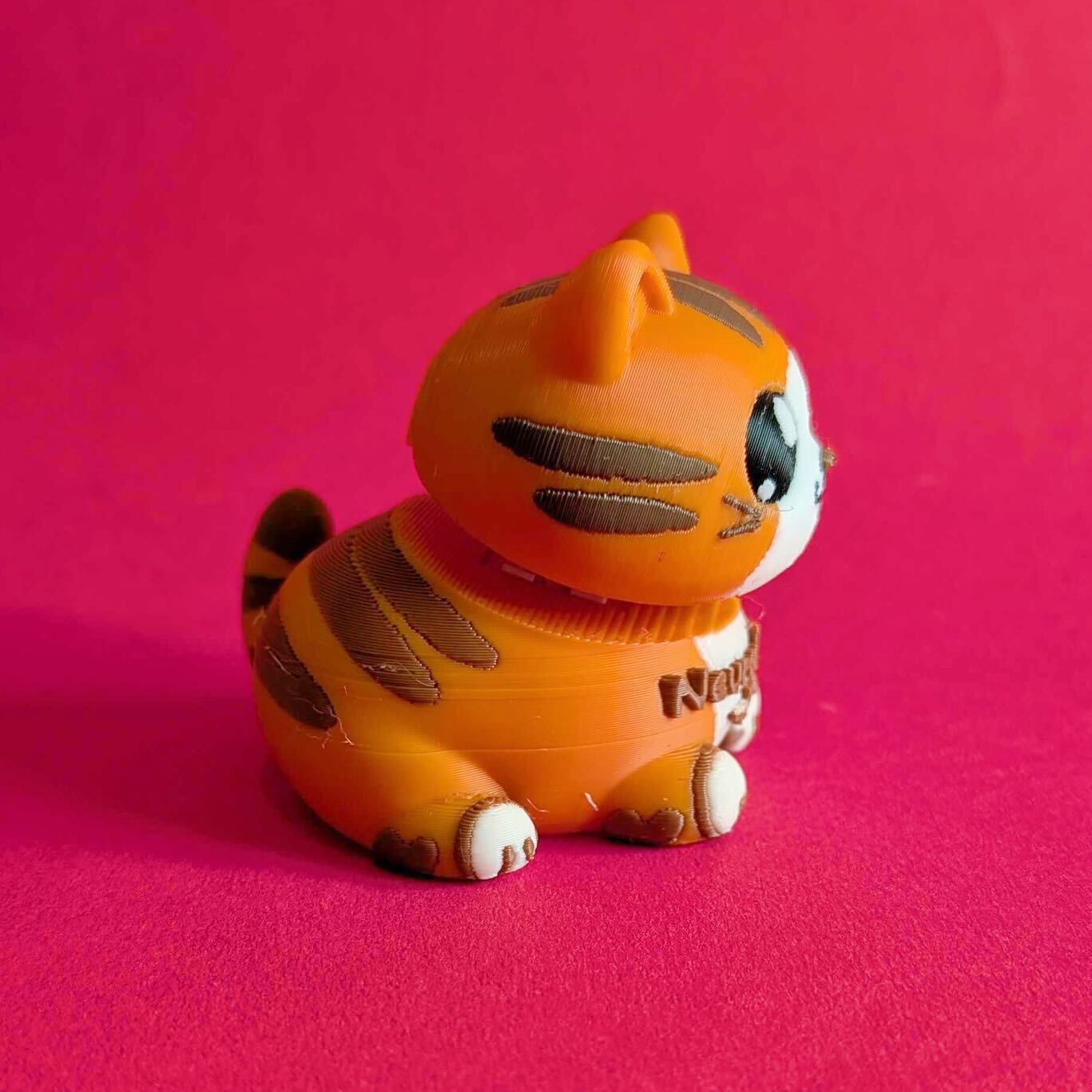 Angled side view of Innabox Neurodiverse Kitty fidget toy with sweet cartoon face, striped body and textured 3D print layers. Palm sized sensory desk buddy with gentle clicker head movement, created to support neurodiversity, autism, anxiety and chronic illness.
