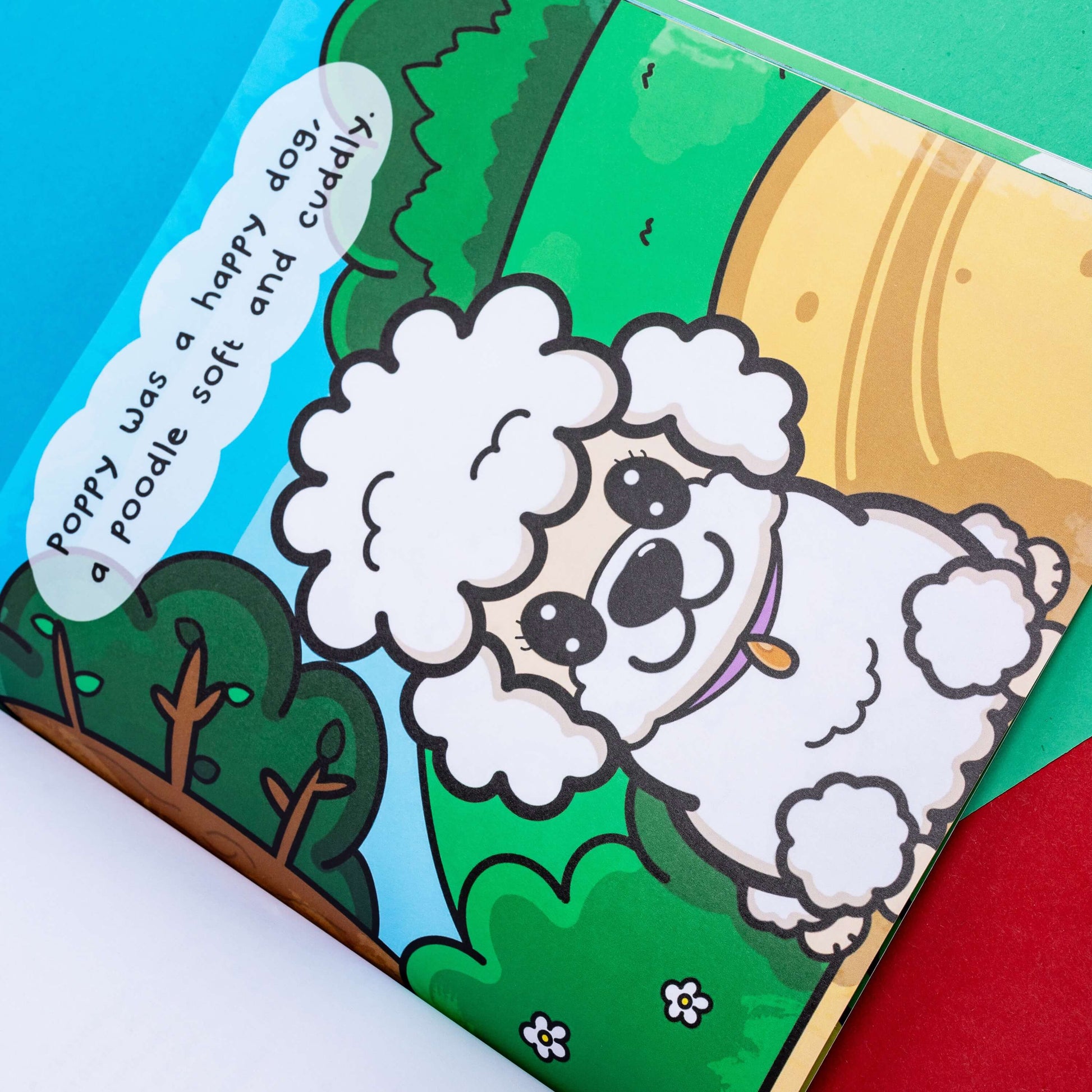 The My Invisible Friends Children's Book on a red, blue and green background. The book is open on a page about poppy the poodle. The hand illustrated book is raising awareness for invisible illnesses.