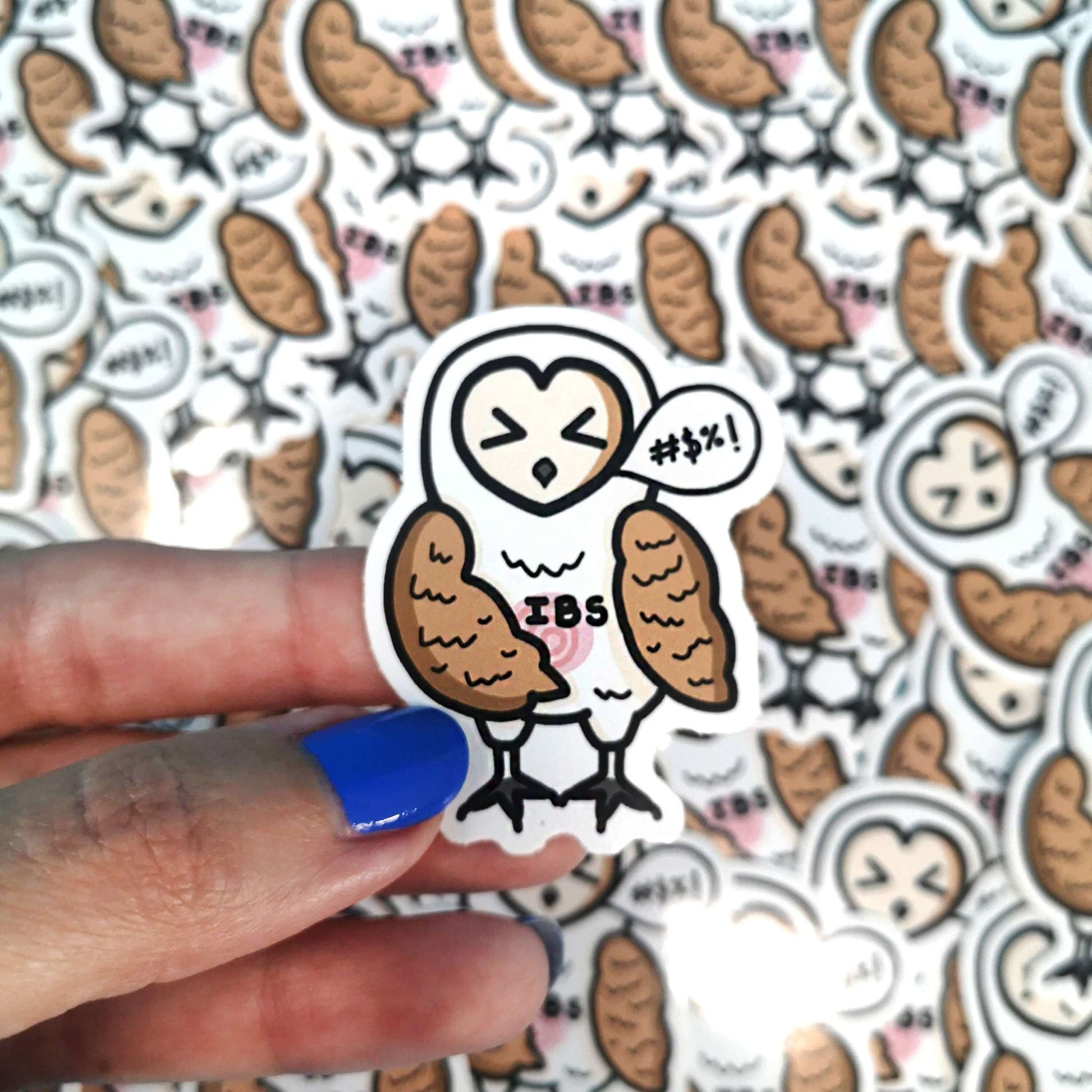 The Irritable Owl Syndrome Sticker - Irritable Bowel Syndrome (IBS) being held over a pile of multiple copies of the same barn owl sticker. The barn owl sticker has its eyes shut with a wing on it's swirling red belly and a speech bubble with swearing symbols inside, across its middle in black text reads 'IBS'. The hand drawn design is raising awareness for irritable bowel syndrome and food intolerances.