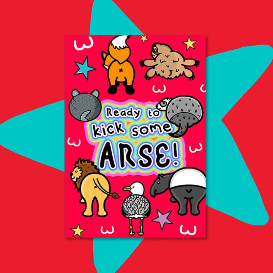 The Ready To Kick Some Arse Postcard on a red and blue star background. The red card print features various animal bums (fox, sloth, chinchilla, badger, lion, seagull and tapir) with white bum outlines, yellow, blue and pink stars and centre rainbow outline text reading 'Ready to kick some arse!'. 