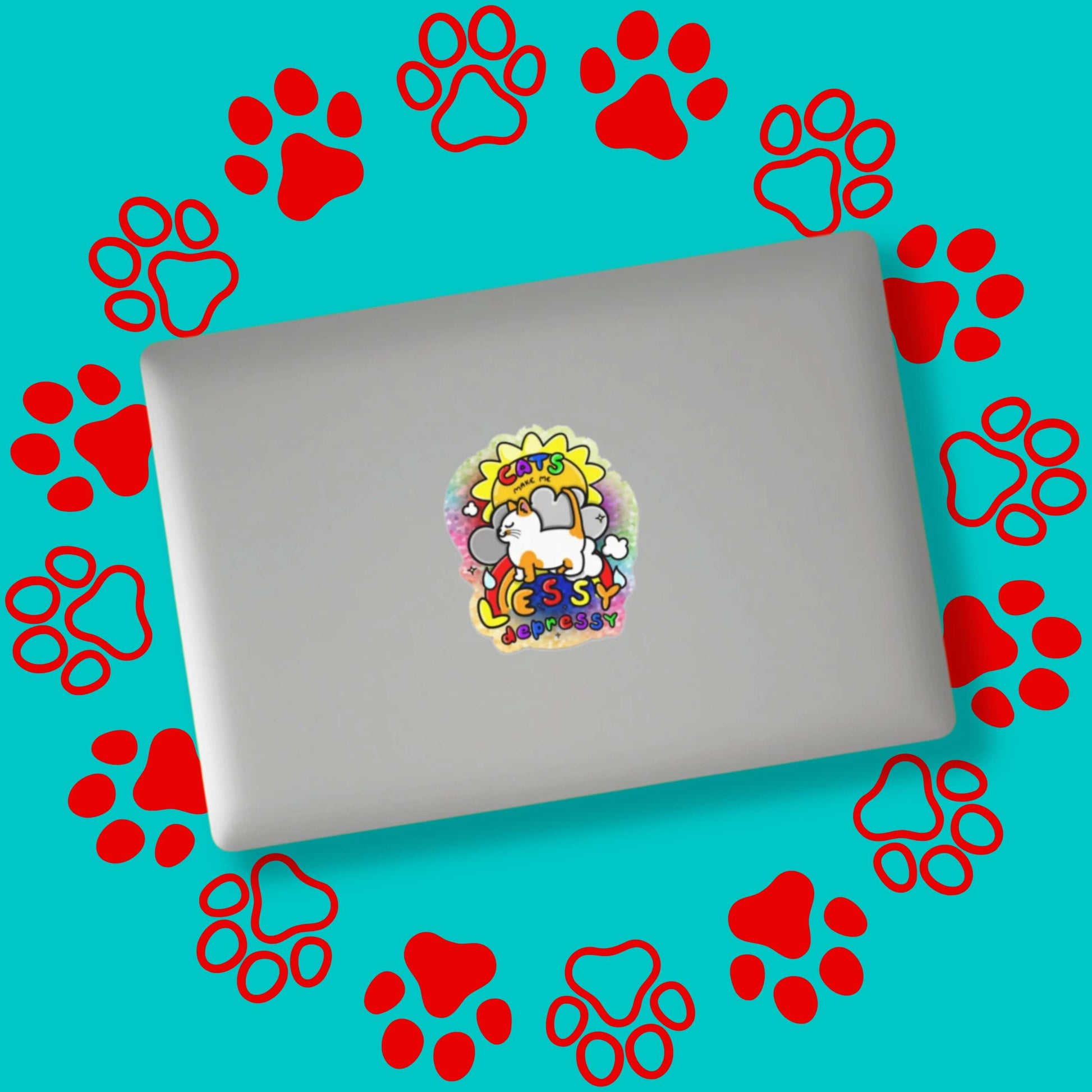The Cats Make Me Lessy Depressy Holographic Glitter Sticker stuck on a silver laptop on a red and blue paw print background. The holographic glittery sticker is of a smiling orange and white cat with a sunshine, raincloud and rainbow underneath, surrounding is rainbow text reading 'cats make me lessy depressy'. Hand drawn design raising awareness for mental health.
