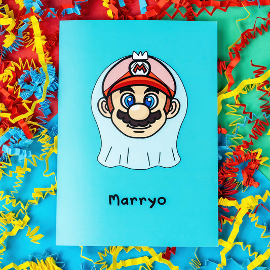 The Marryo - Mario Engagement Wedding Card on a red, blue and green background with red, yellow and blue crinkle card confetti. The blue a6 congratulations card features a smiling nintendo mario character head wearing a white bridal wedding veil, underneath him is black text reading 'Marryo'.