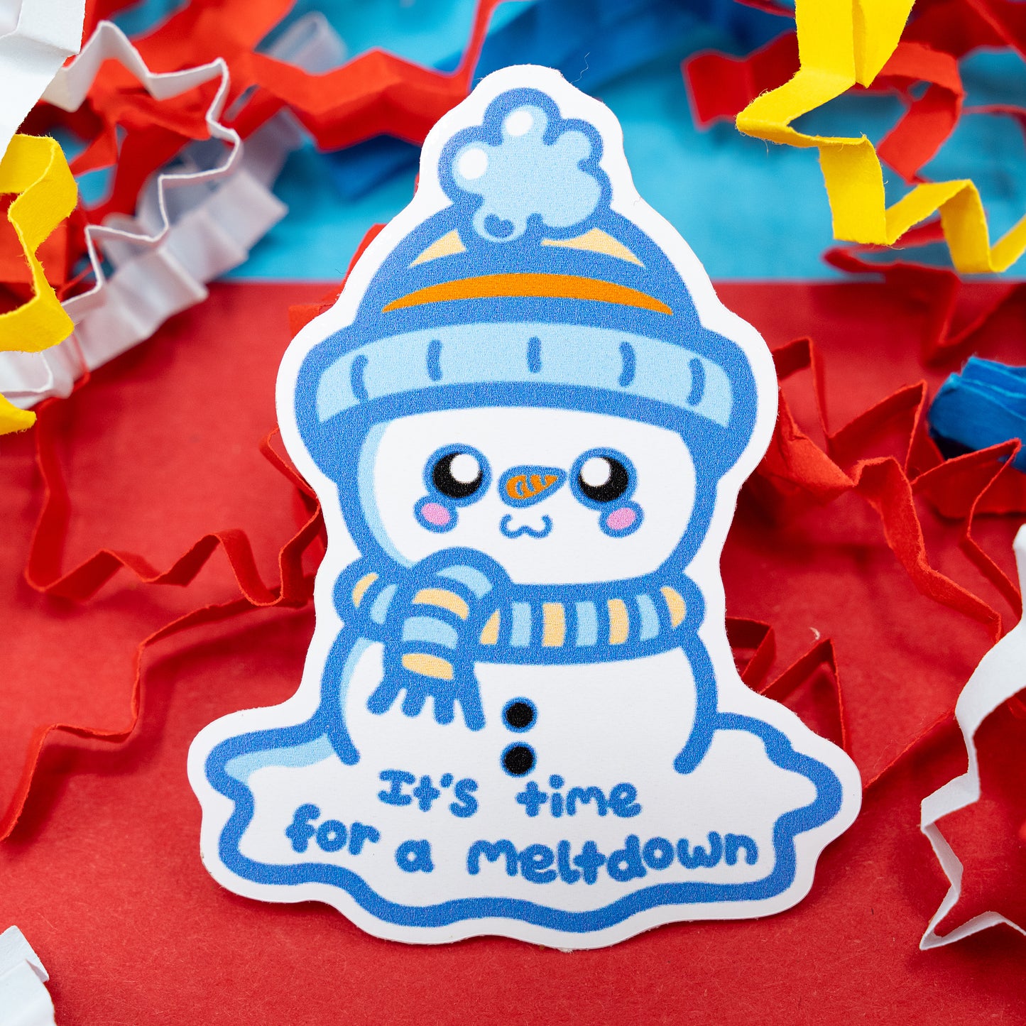 “It’s Time for a Meltdown” vinyl sticker by Innabox featuring a cute snowman in a blue hat and scarf, melting with a cheerful smile. Surrounded by colourful confetti on a red background. Glossy, waterproof sticker designed to raise awareness for sensory overload, stress, and self-care moments.