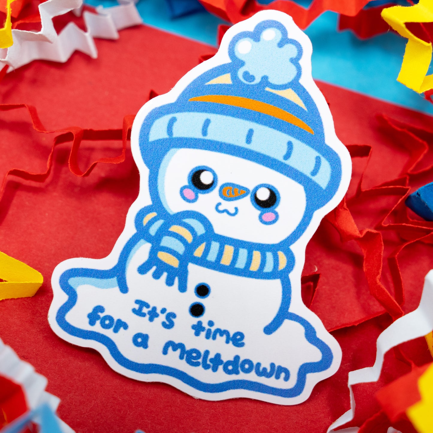 Close-up of “It’s Time for a Meltdown” snowman sticker by Innabox, showing a cute melting snowman with a blue hat and scarf on a red surface. A waterproof gloss vinyl sticker symbolising kindness, self-compassion, and neurodivergent awareness.