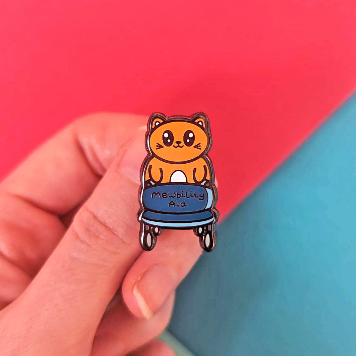The Mewbility Aid Cat Enamel Pin - Mobility Aid held over a red and blue background. An orange smiling cat walking upright with a blue mobility aid, across the walking chair reads 'mewbility aid'. The hand drawn designs is raising awareness for mobility aids.