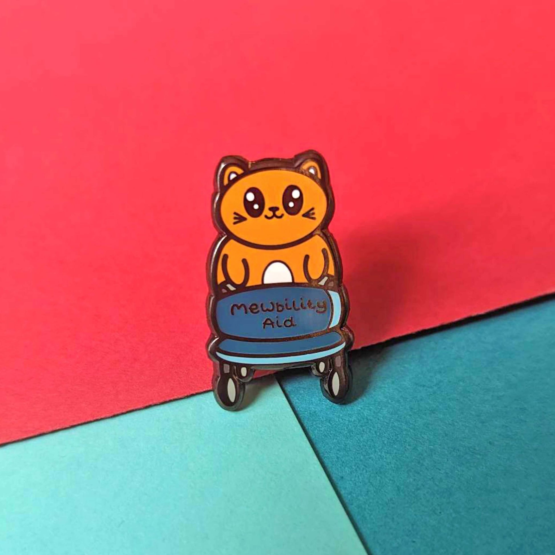 The Mewbility Aid Cat Enamel Pin - Mobility Aid on a red and blue background. An orange smiling cat walking upright with a blue mobility aid, across the walking chair reads 'mewbility aid'. The hand drawn designs is raising awareness for mobility aids.