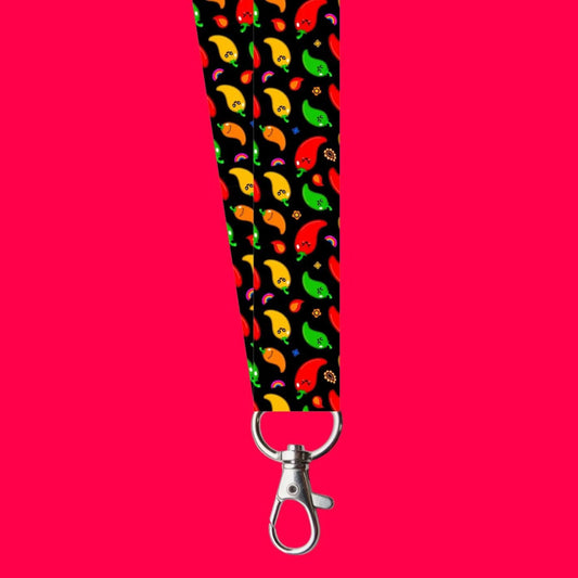 The Neuro-Spicy Lanyard on a red background. The black polyester lanyard has red, green, orange and yellow chilli peppers with rainbows and flames all over with a silver lobster clip at the end. The hand drawn design is raising awareness for neurodivergent people.