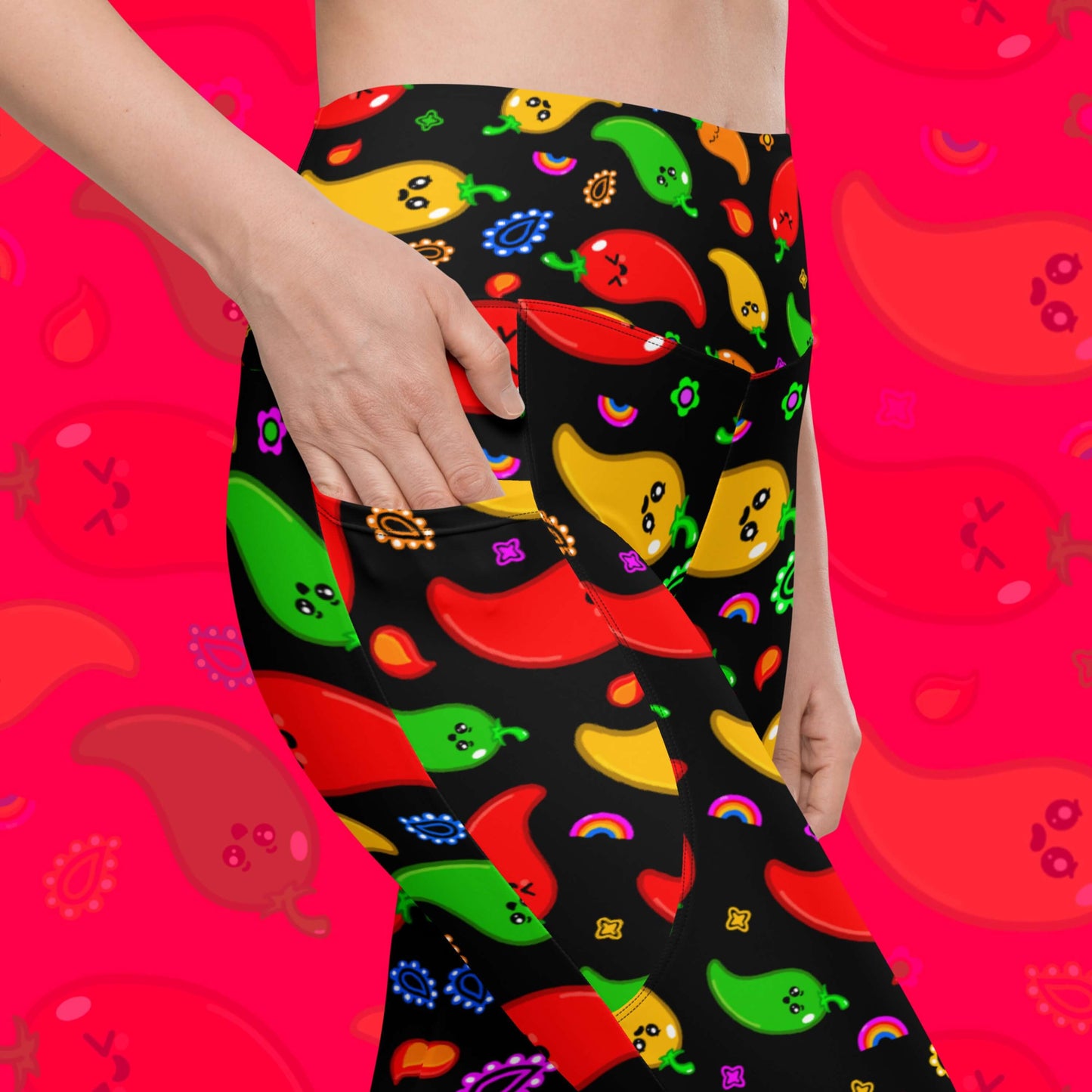 Black leggings with pockets with red, green, orange and yellow chilli peppers with cute faces on and various cute doodles around them shown on a model who has one hand in the leggings picket. The background of the photo is a faded close up of the print. The hand drawn design is raising awareness for neurodiversity. 