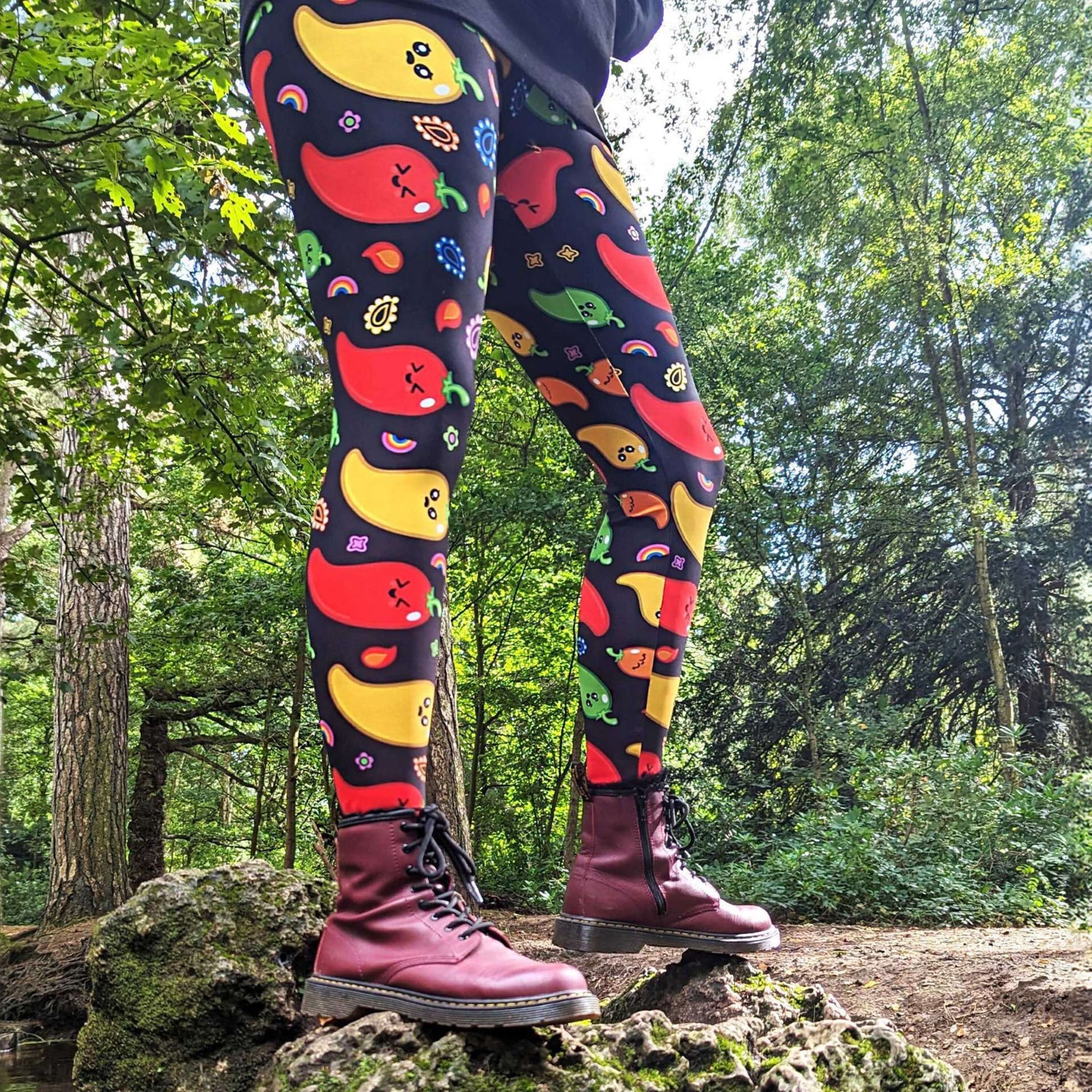 A person standing on a rock wearing Black leggings with red, green, orange and yellow chilli peppers with cute faces on and various cute doodles around them. The hand drawn design is raising awareness for neurodiversity.