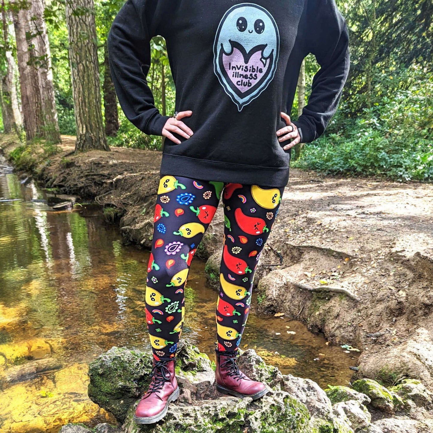 A person standing on a rock wearing Black leggings with red, green, orange and yellow chilli peppers with cute faces on and various cute doodles around them. The hand drawn design is raising awareness for neurodiversity.