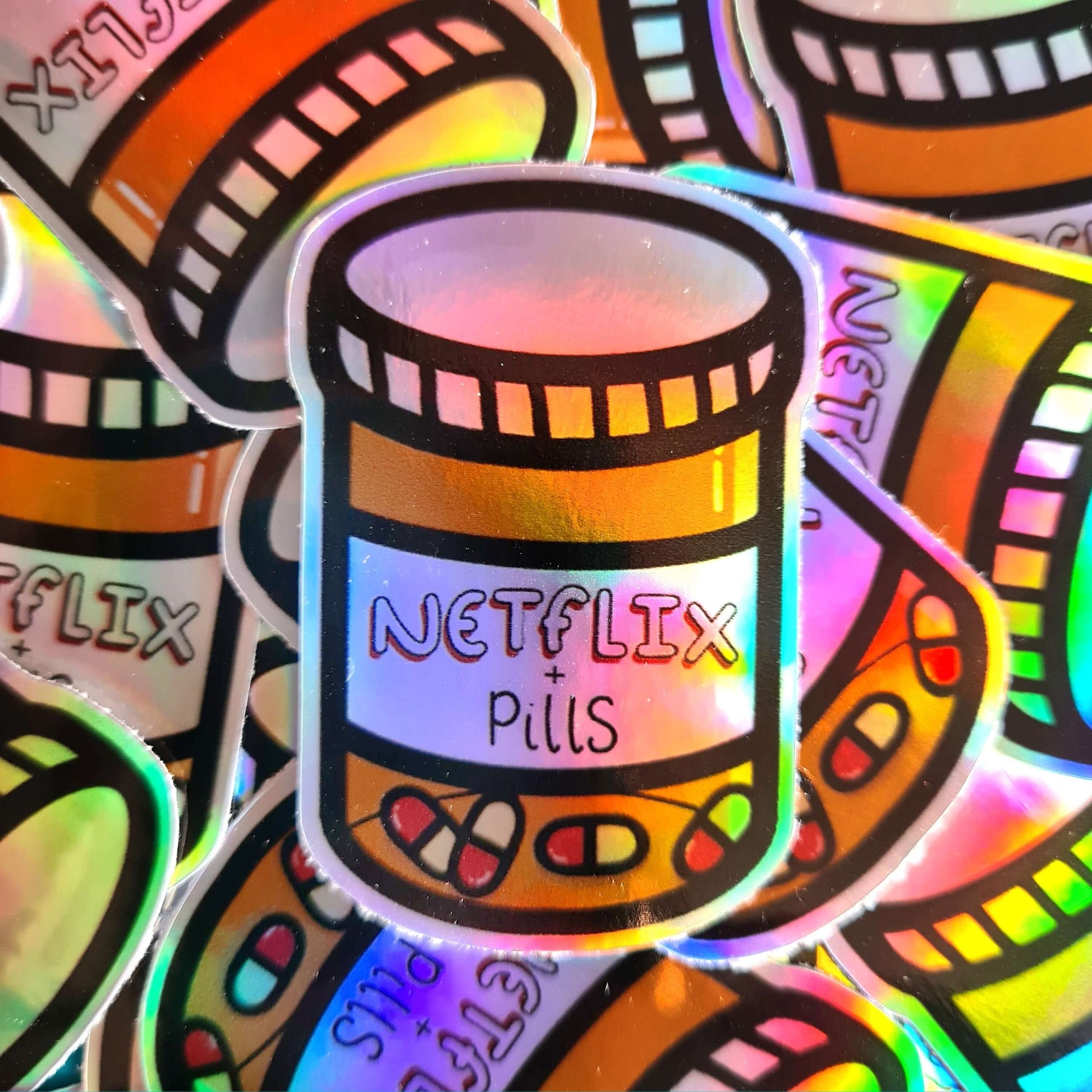 The Netflix & Pills Holographic Sticker on multiple copies of the same sticker. The holographic shiny rainbow pill bottle sticker filled with red and white tablets with a label that reads 'netflix + pills'. A cheeky hand drawn design to raise awareness for hidden disability prescriptions.
