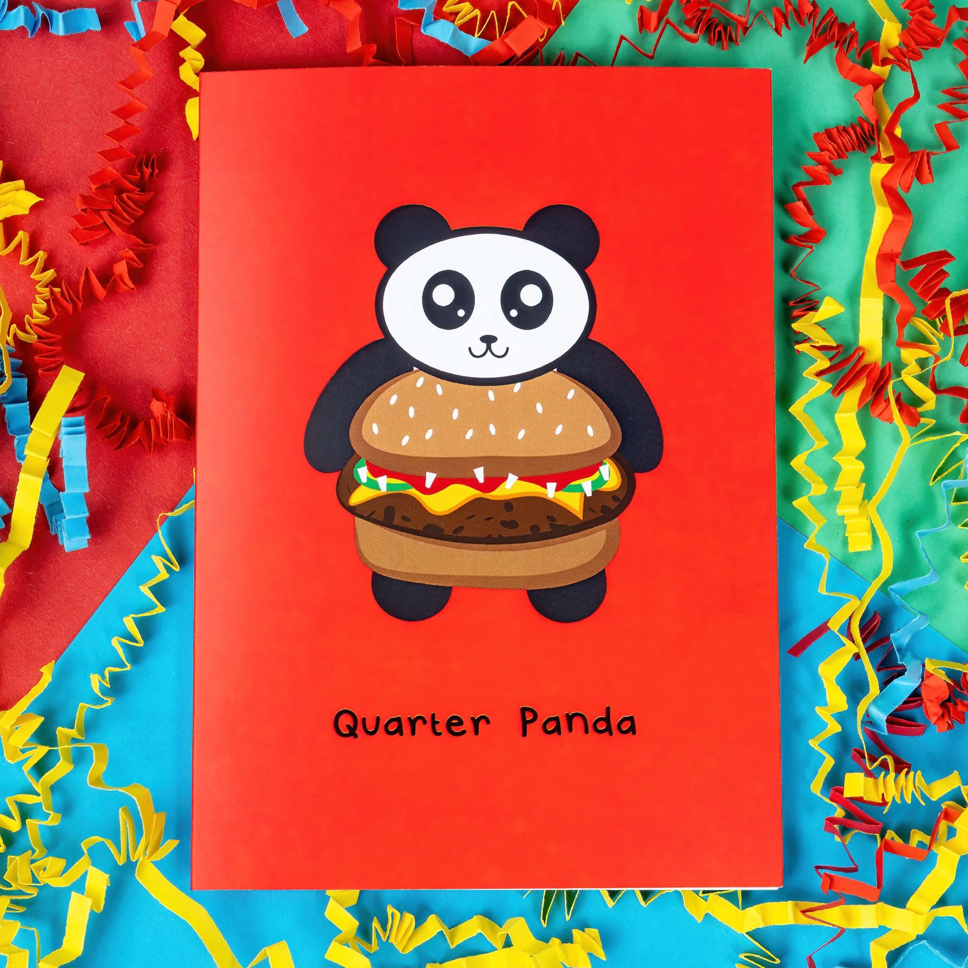 The Quarter Panda Burger Card on a red, blue and green background with yellow, red and blue crinkle card confetti. The red a6 greeting card has a smiling panda with its body being a seeded bun burger. Underneath in black reads 'quarter panda'.