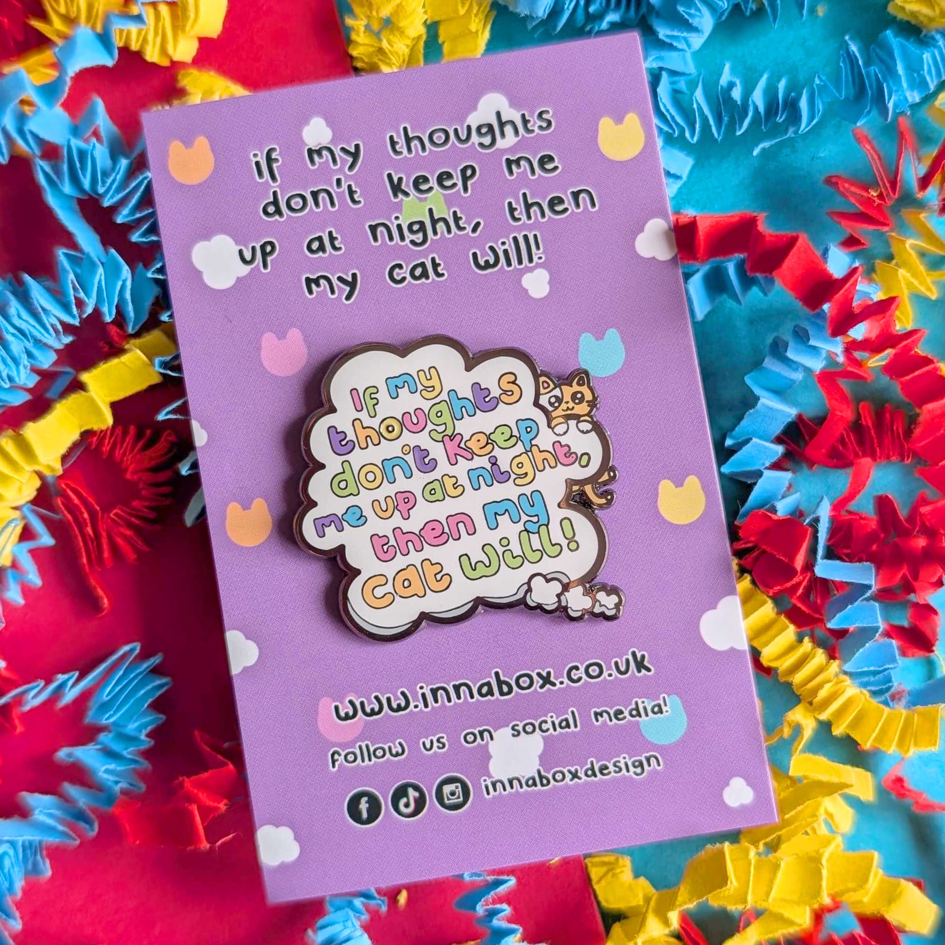 Innabox enamel pin reading “If my thoughts don’t keep me up at night, then my cat will” displayed on a lilac backing card with pastel cat and cloud details, surrounded by bright blue, yellow and red crinkle paper. Cute mental health inspired accessory for cat lovers.
