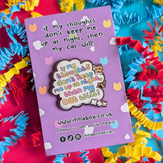 Innabox enamel pin reading “If my thoughts don’t keep me up at night, then my cat will” displayed on a lilac backing card with pastel cat and cloud details, surrounded by bright blue, yellow and red crinkle paper. Cute mental health inspired accessory for cat lovers.
