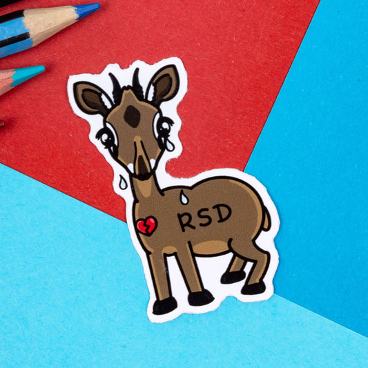 The Rejection Senstive Dik-sphoria Dik-Dik Sticker - Rejection Sensitive Dysphoria RSD on a red and blue background with colouring pencils. The brown dik-dik deer is crying with a broken red heart and the initials 'RSD' across its back. The hand drawn design is raising awareness for Rejection Sensitivity Disorder.