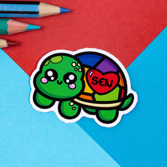 The Speshell Educational Needs Tortoise Sticker - Special Educational Needs SEN on a red and blue background. The green smiling tortoise has a rainbow shell with a red heart and black text inside reading 'SEN'. The hand drawn design is raising awareness for Special Educational Needs SEN.
