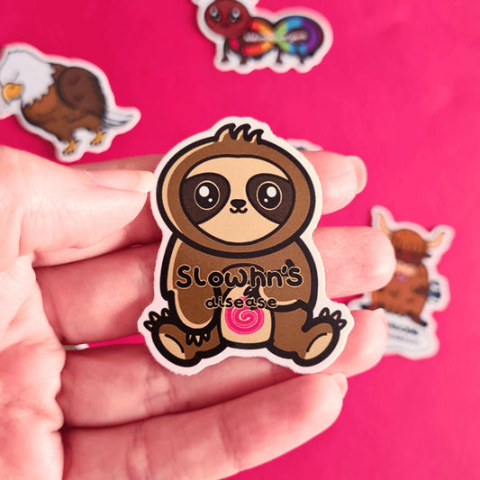 The Slowhn's Disease Sloth Sticker - Crohn's Disease being held over a red background with other innabox stickers. The sloth shape sticker is smiling sat down clutching its tummy that has a red swirl and text reading 'slowhn's disease'. The design is raising awareness for crohn's disease.