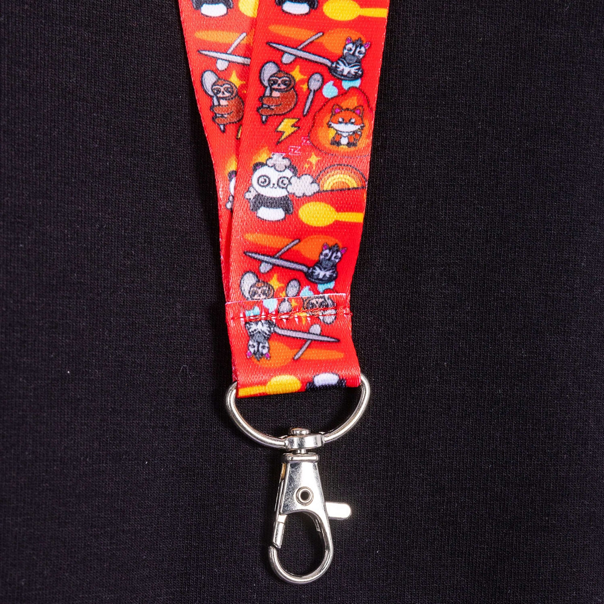 close up of the red lanyard featuring Spoonie characters by Innabox, spoons and rainbows with the metal clasp hanging from it against a black background