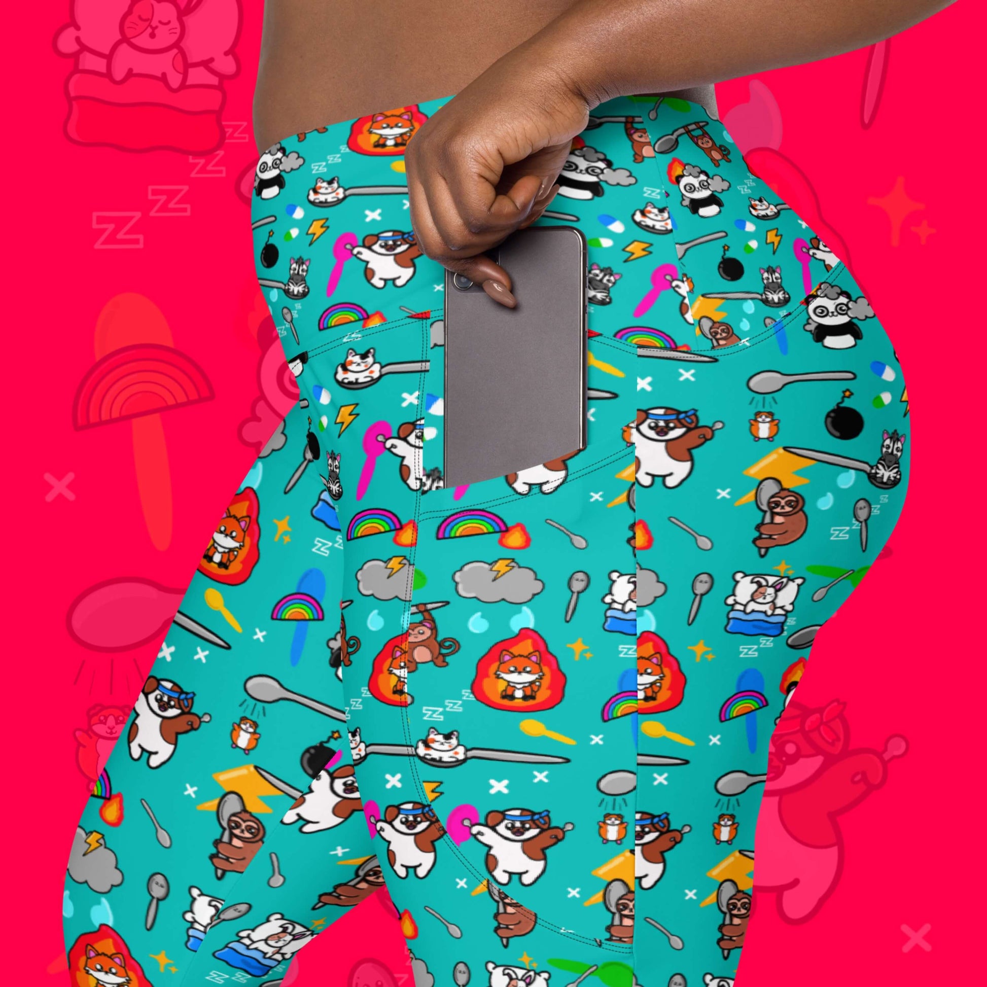 The Spoonie Leggings with Pockets modelled by a femme person putting a silver phone in the pocket on a red background with a faded version of the print in the background. The blue leggings feature various invisible illness themed animals, rainbows, spoons, sparkles, flames, pills and lightning bolts. Raising awareness for hidden disabilities.