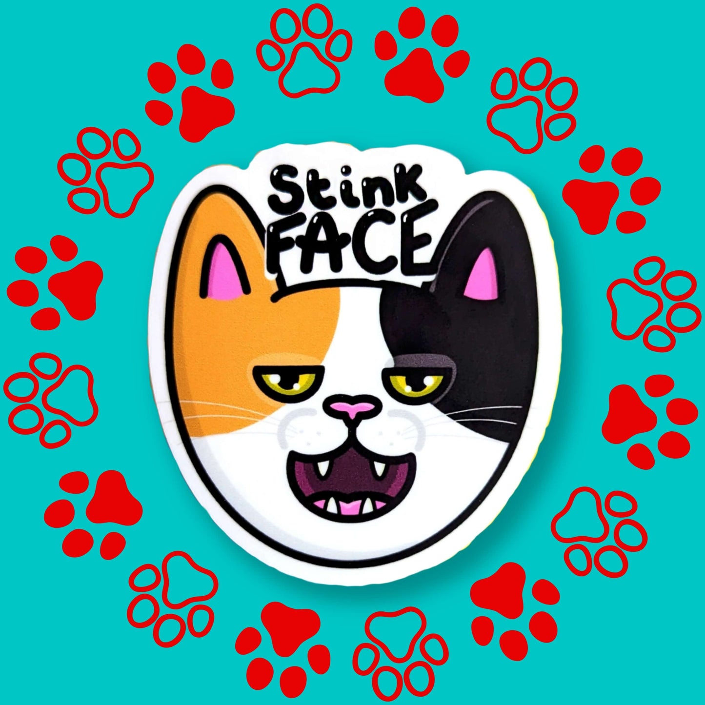 The Stink Face Cat Sticker on a red and blue paw print background. The orange and black cat head sticker is smiling with a smug look on its face and black text above reading 'stink face'. 