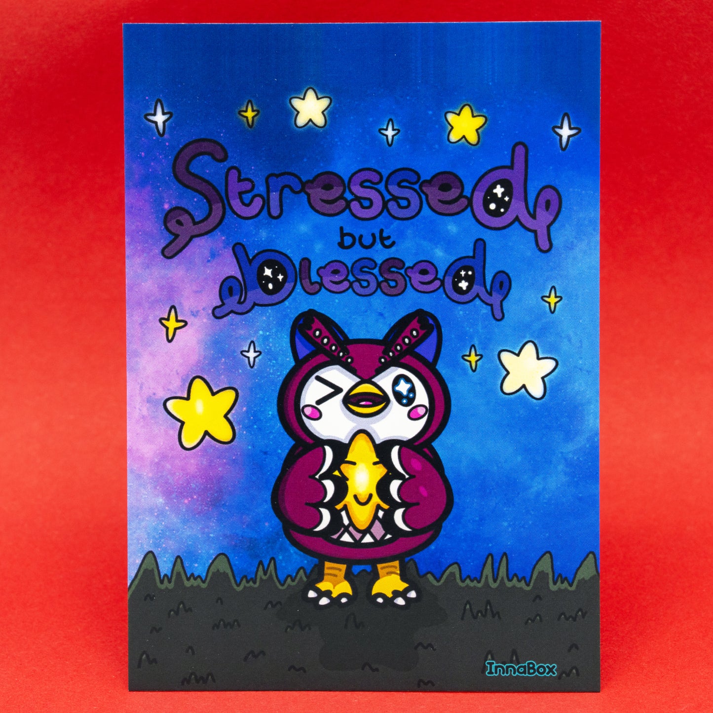 A colourful Innabox Stressed But Blessed Celeste Postcard featuring a cute owl character holding a glowing star fragment. The background shows a dreamy night sky with bright yellow stars and soft purple and blue tones. This disability inspired uplifting postcard is printed on 350gsm silk board and is blank on the reverse. Ideal for gifting, collecting, or displaying as positive art.