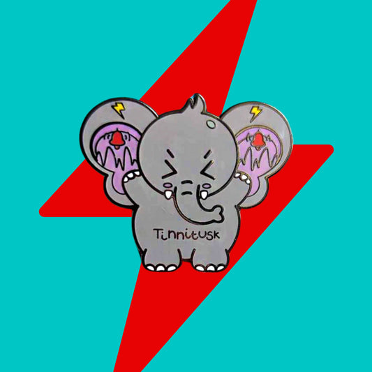 Tinnitus Enamel Pin on a blue and red background. A grey elephant shaped enamel pin with big ears with purple on the inside of them and black squiggly lines with red ringing alarm bells above the lines and yellow lightening bolts above the bells. The elephant has its eyes screwed shut and its arms up. 'Tinnitusk' is written in black across its middle.