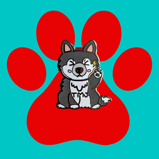 The Tempawromandibular Disorder Dog Enamel Pin - Temporomandibular Disorder TMJ on a red and blue background. The grey husky dog shaped enamel pin has a pained face with shut eyes, one paw up by its jaw with a yellow lightning bolt and black text across its chest reading 'TMJ'. The hand drawn design is raising awareness for Temporomandibular Disorder TMJ.