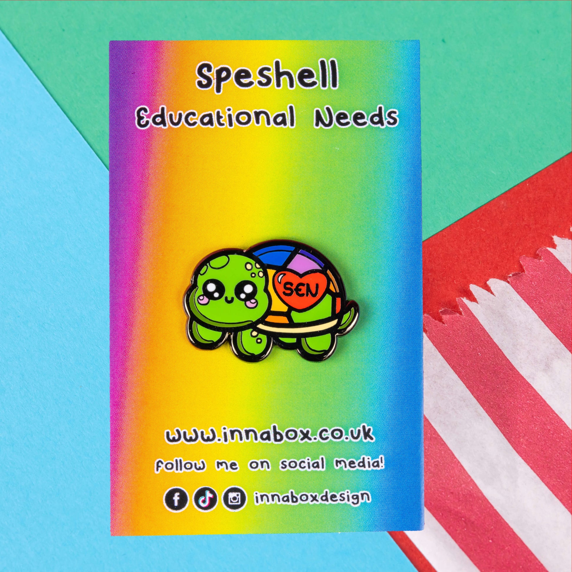The Speshell Educational Needs Enamel Pin - SEN - Special Educational Needs on a rainbow backing card with black text. A rainbow shell kawaii cute style tortoise with pink cheeks and sparkling eyes, on its shell is a red heart with 'SEN' in the middle. The pin design is raising awareness for SEN Special Educational Needs.