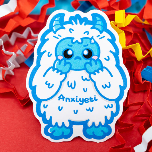 Anxi-Yeti vinyl sticker by Innabox featuring a cute blue and white anxious yeti with blushing cheeks and the word “Anxiyeti” on its body. Surrounded by bright red, yellow, and white confetti paper. Glossy finish sticker designed to raise awareness for anxiety, chronic illness and hidden disabilities.