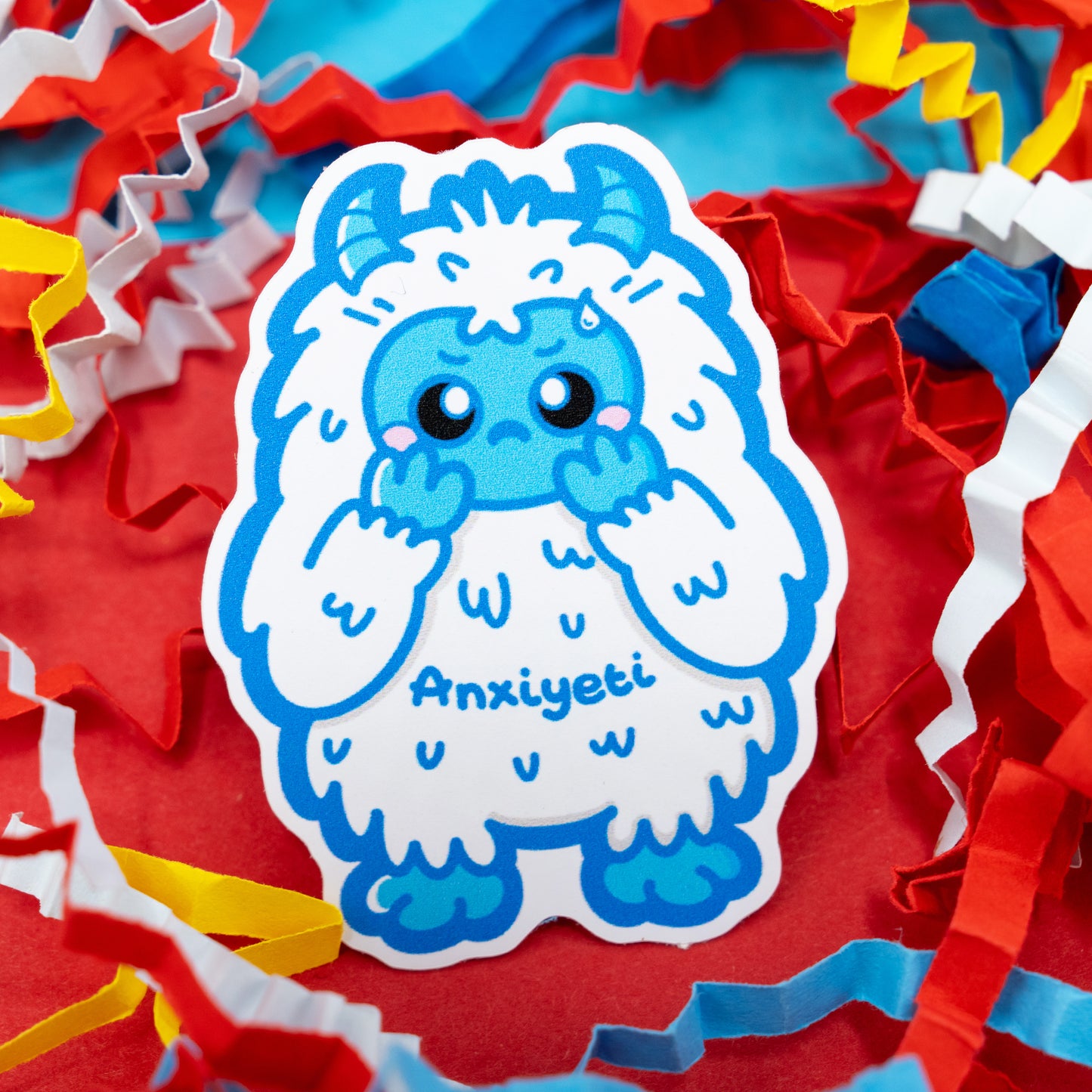 Anxi-Yeti vinyl sticker by Innabox showing a nervous blue yeti character on a red background with colourful confetti. Gloss vinyl anxiety awareness sticker that’s waterproof, durable, and perfect for decorating laptops, journals, or water bottles.