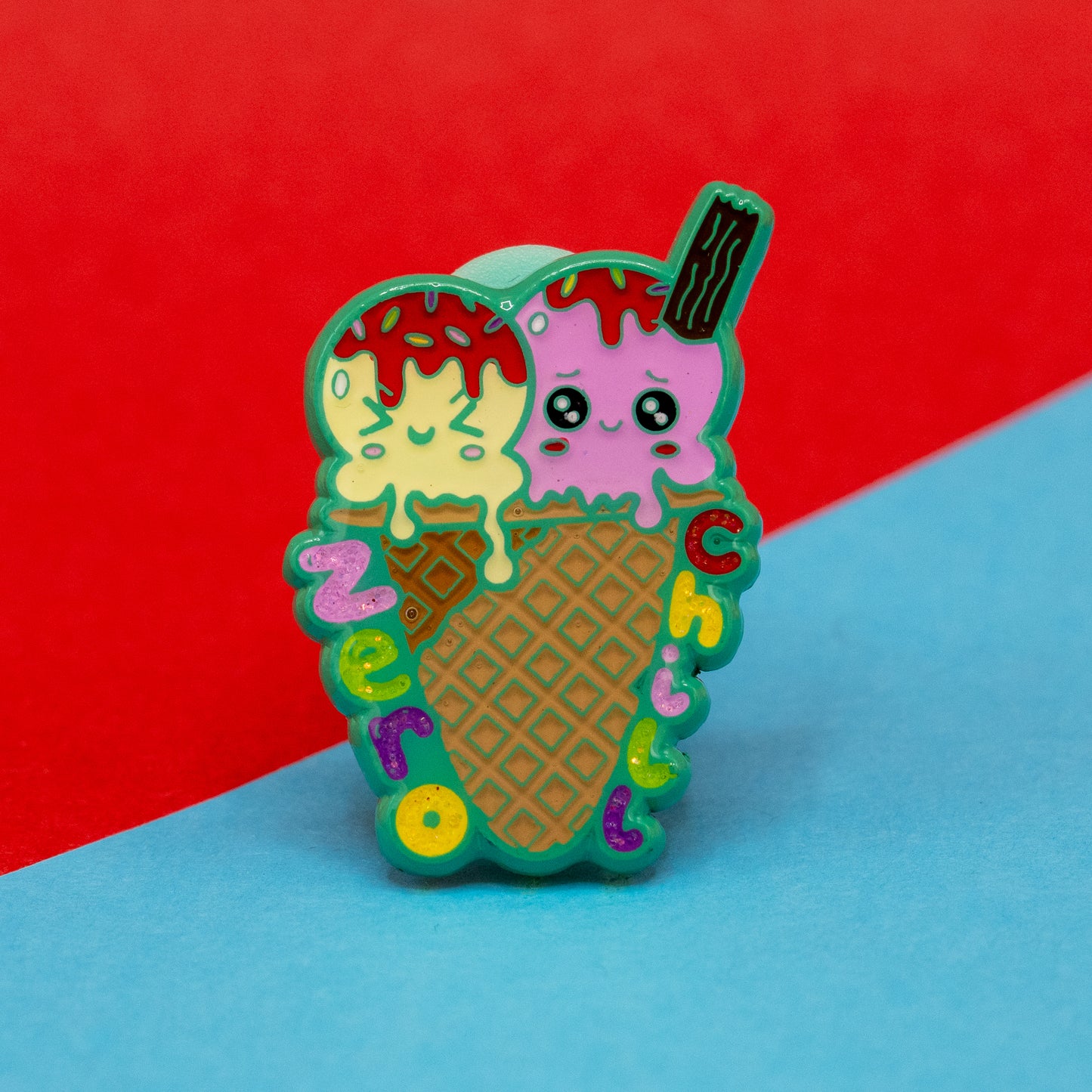 Close-up of the Zero Chill Ice-cream Cone Enamel Pin by Innabox. The pin features pastel yellow and pink ice cream scoops with expressive cartoon faces in a brown waffle cone, with rainbow-coloured letters spelling “Zero Chill.” Includes a small flake and glossy enamel finish. A cheerful pin created to raise awareness for hidden disabilities.
