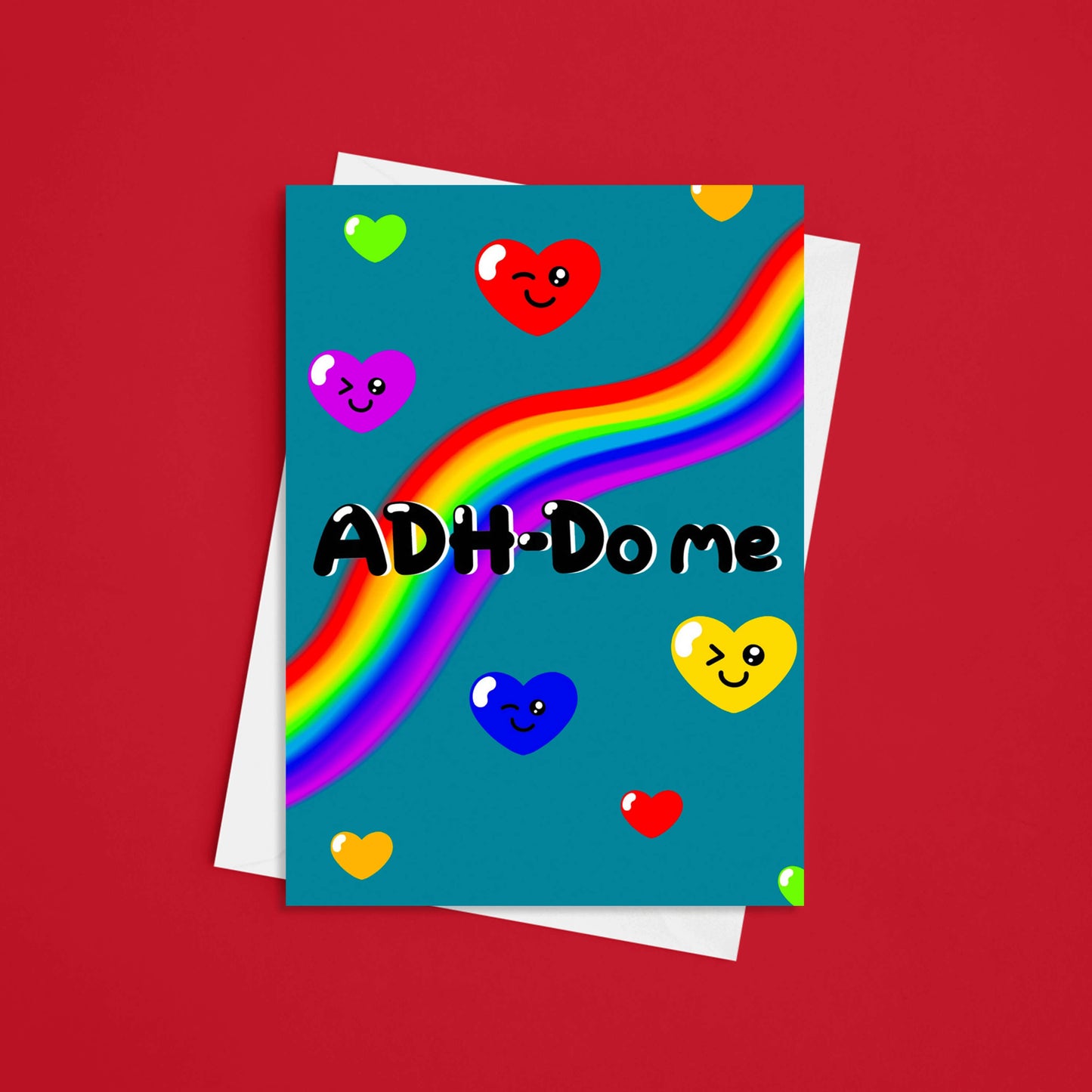 a sky blue greeting card with a rainbow going across it with different coloured love hearts with winky faces dotted around it. 'ADH-Do me' is written in big black letters across the card. The cards pairing white envelope is sat underneath it The background of the photo is red. Inspired by neurodivergent disorders.