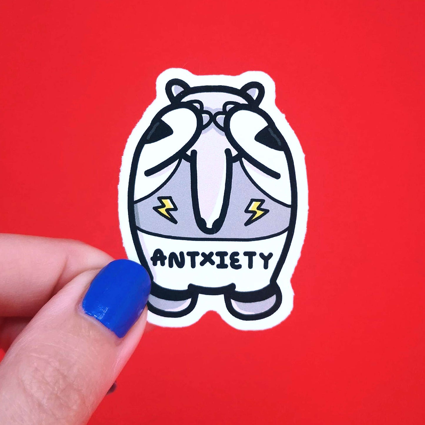 Antxiety Sticker Anxiety being held over a red background. Sticker is a grey and white anteater with yellow lightning bolts and the word antxiety across its belly. The sticker is designed to raise awareness for anxiety disorders and anxious emotions.
