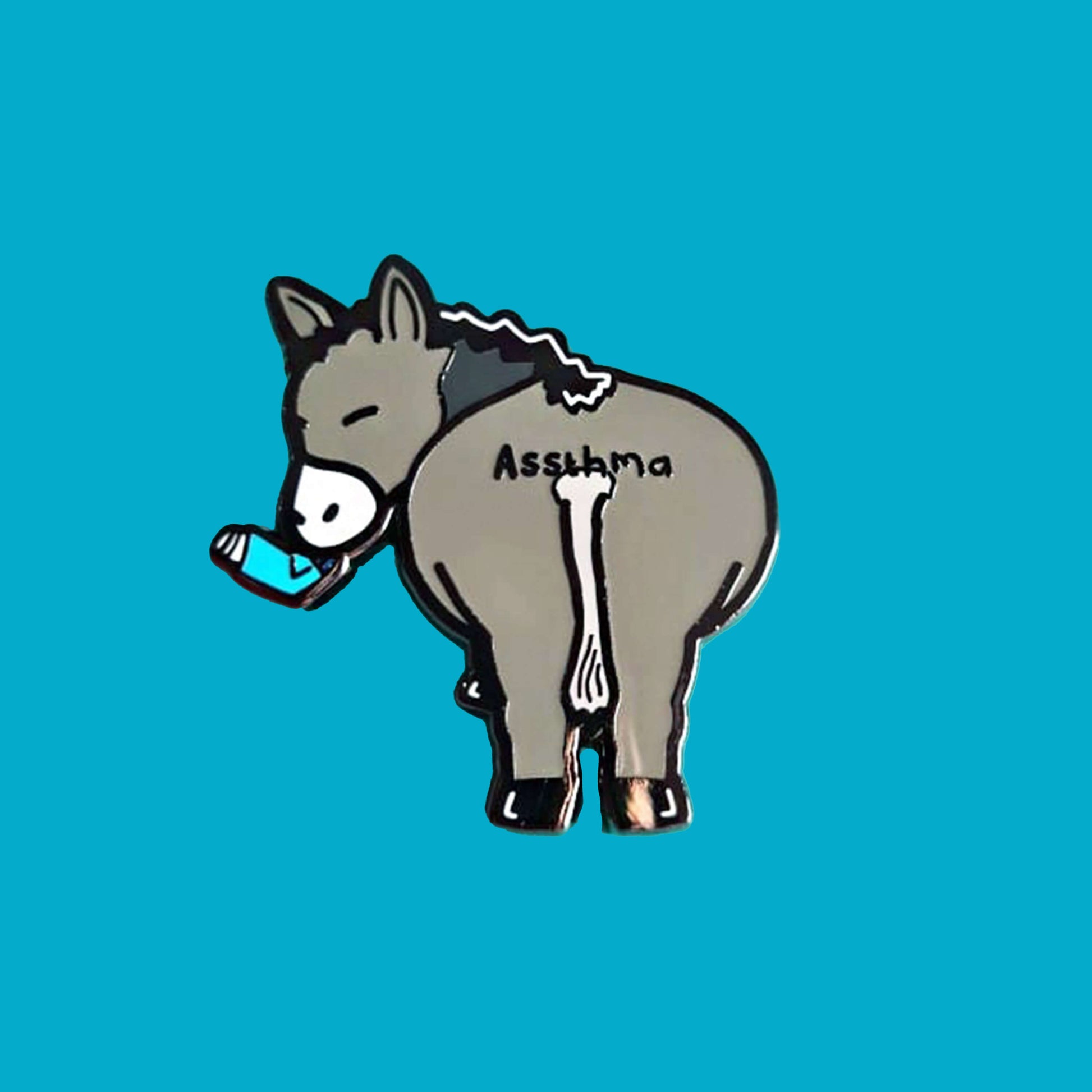Assthma Enamel Pin - Asthma on a blue background. A grey donkey ass showing its behind with a blue asthma pump in its mouth and the word Assthma across its behind. The pin is designed to raise awareness for asthma.