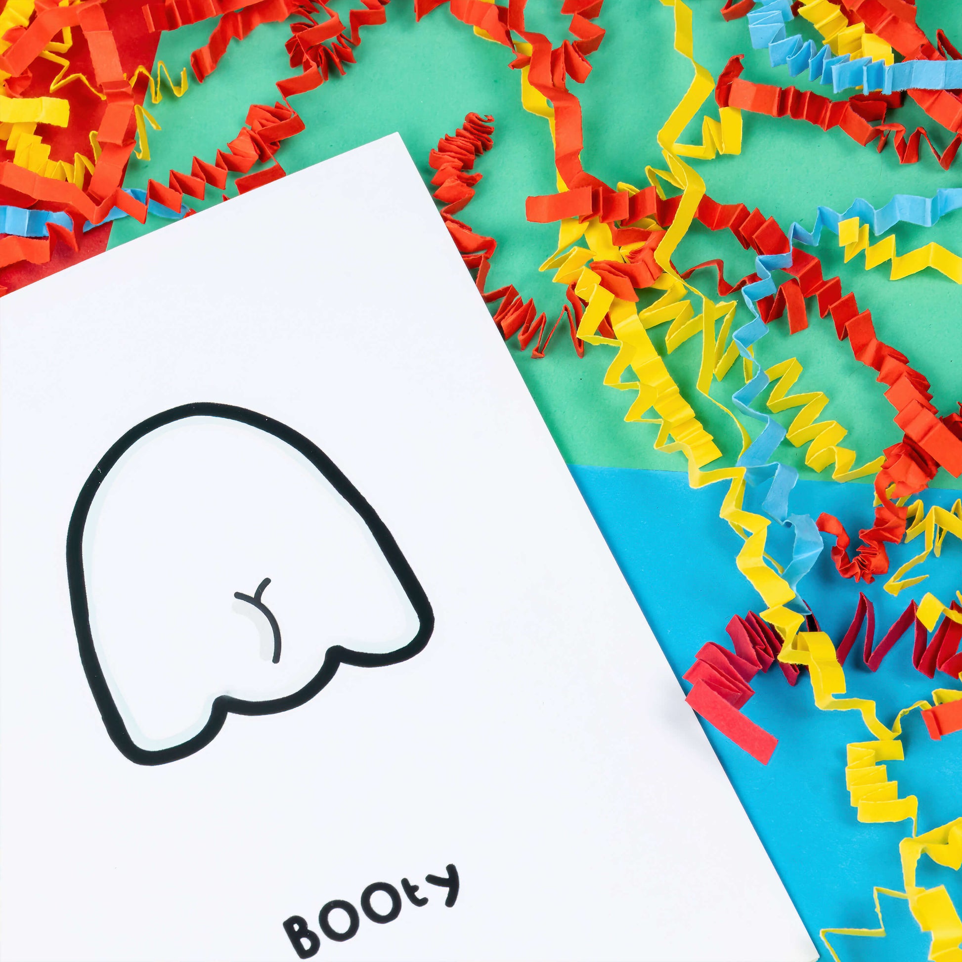 Close up of The Booty Ghost a6 card on a blue, red and green background with yellow, blue and red crinkle card confetti. A white greeting card with an illustration of the back of a ghost with a bum crack. The word 'BOOty" is written in black underneath the drawing.
