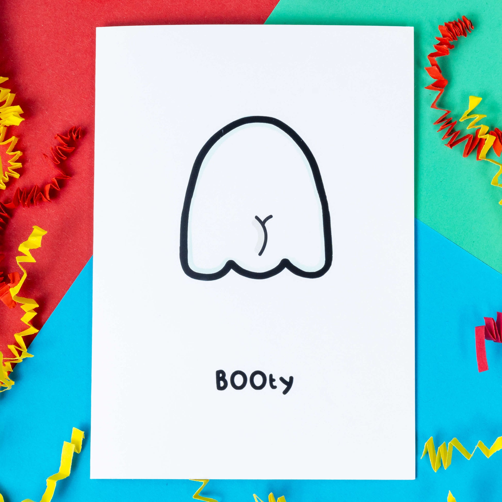 The Booty Ghost a6 card on a blue, red and green background with yellow and red crinkle card confetti. A white greeting card with an illustration of the back of a ghost with a bum crack. The word 'BOOty" is written in black underneath the drawing.