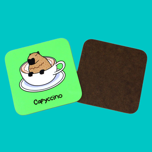 The Capyccino - Capybara Cappuccino Coaster on a blue background. The wooden green coaster features a cute brown capybara sat peeking over a cappuccino in a white mug and saucer, underneath reads capyccino in black. To the right shows the back of the coaster which is plain dark brown wood.