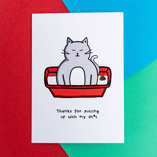 A white card with a drawing of a grey cat sat in a litter box with a poop in it with text underneath that says, thanks for putting up with my sh*t. The a6 thank you card is laying on a red, blue and green background.