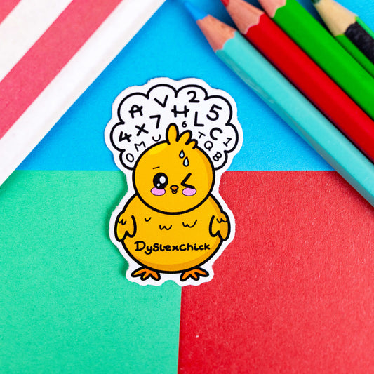 Dyslexchick Sticker - Dyslexic on a red, blue and green background with colouring pencils and red stripe candy bag. A yellow confused chick shaped vinyl sticker with a thought bubble above its head full of letters and numbers with 'dyslexchick' written across its middle. The hand drawn design is raising awareness for dyslexia.
