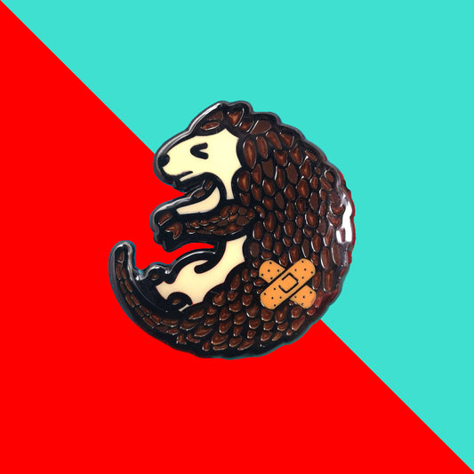 The Chronic Paingolin Enamel Pin - Chronic Pain on a blue and red background. The pangolin shaped pin has a frustrated expression whilst curled up with a double cross bandaid plaster on its side. The design was created to raise awareness for chronic pain.