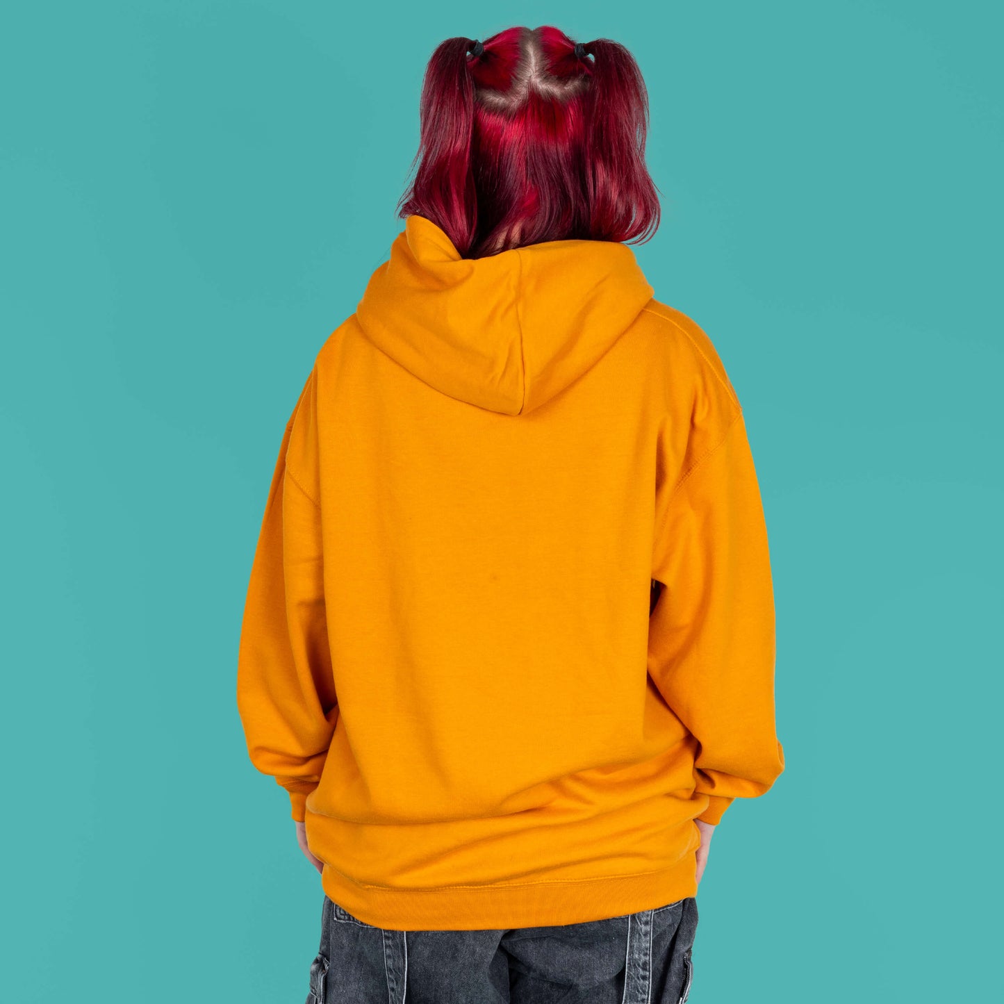 The Chronic Over Sharer Pumpkin Orange Hoodie modelled on Flo, a red haired alternative model, in front of a blue background. She is facing away from camera to highlight the plain orange back. The design was created to raise awareness for neurodivergent disorders such as ADHD.