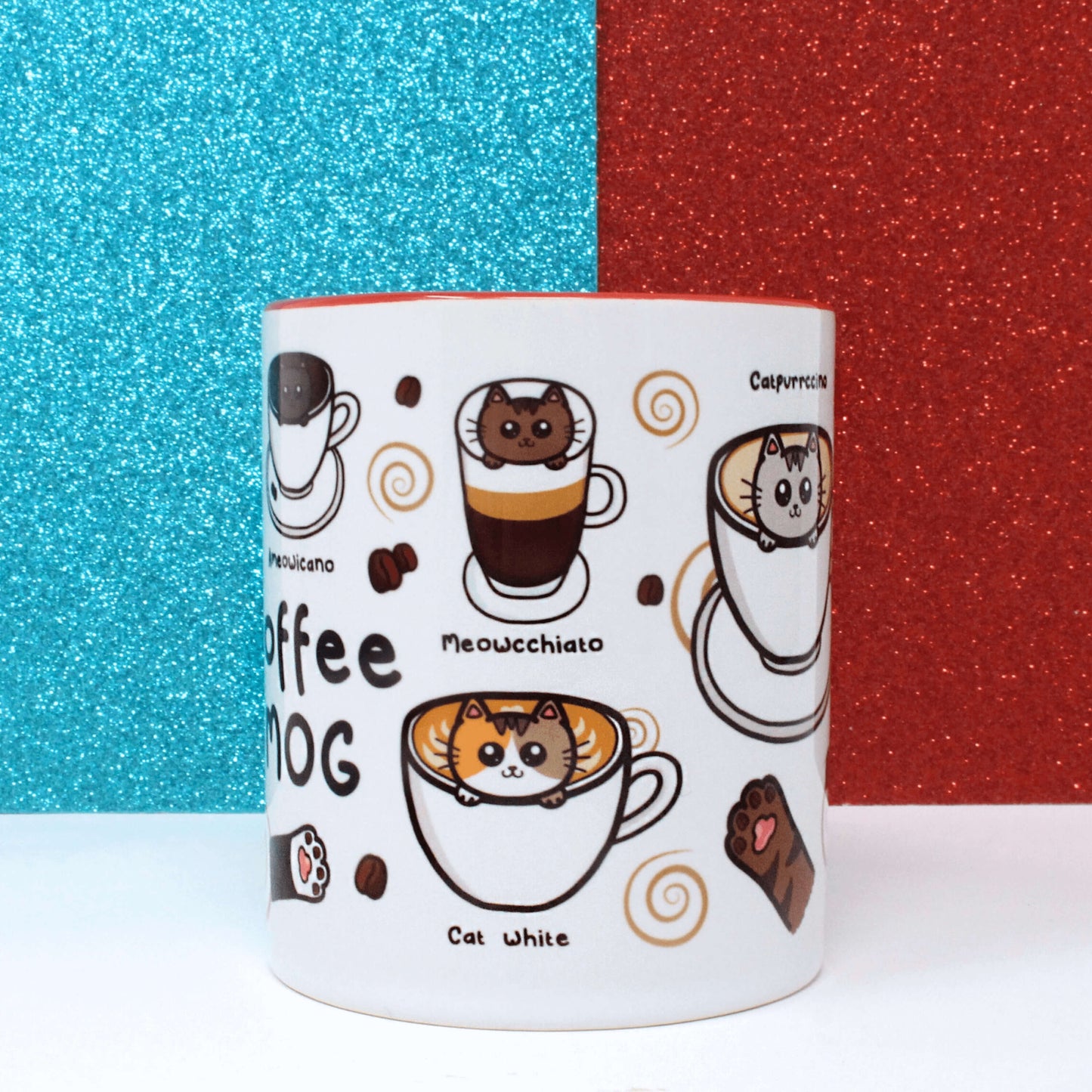 The Coffee Mog Cat Mug on a white table with a red and blue glitter background. The cat themed white coffee mug with red inner and handle is facing forward to show illustrations of cat paw toe coffee beans, meowcchiato (a brown cat in a mochiatto), cat white (a tortoiseshell cat in a flat white), catpurrccino (a grey cat in a cappuccino) with coffee beans and brown swirls.